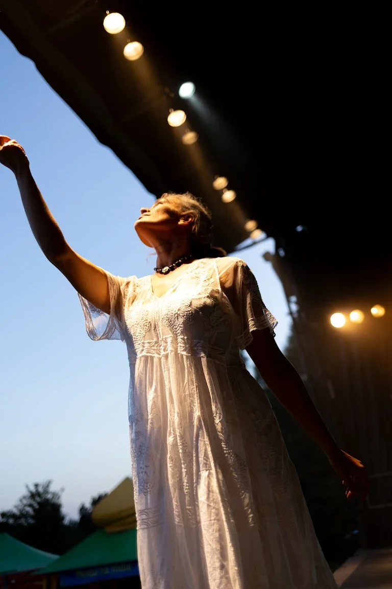 A performer in white reaches toward the light at golden hour